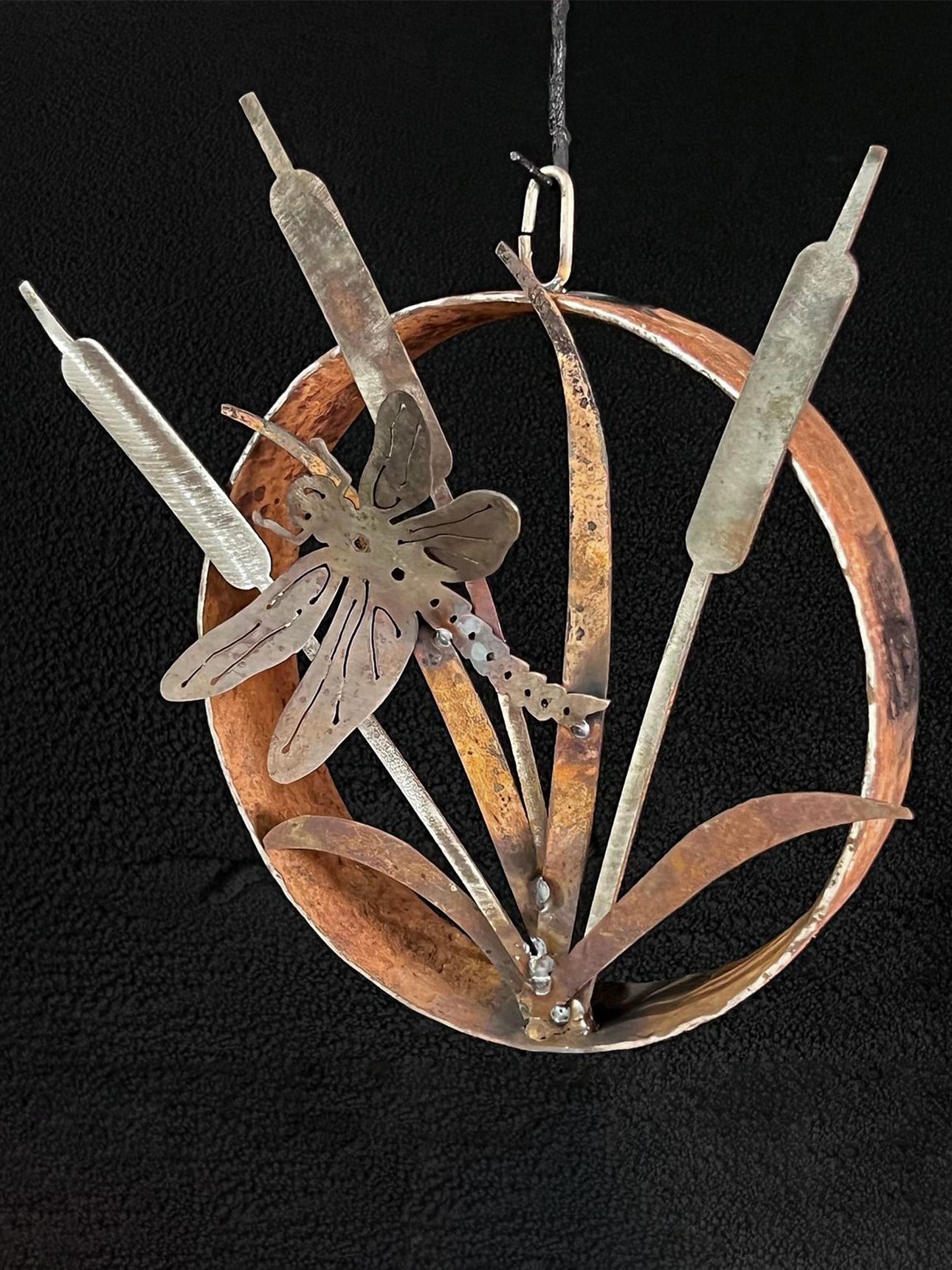 An artistic metal sculpture featuring a dragonfly resting on a cattail, highlighting the beauty of nature in a creative form