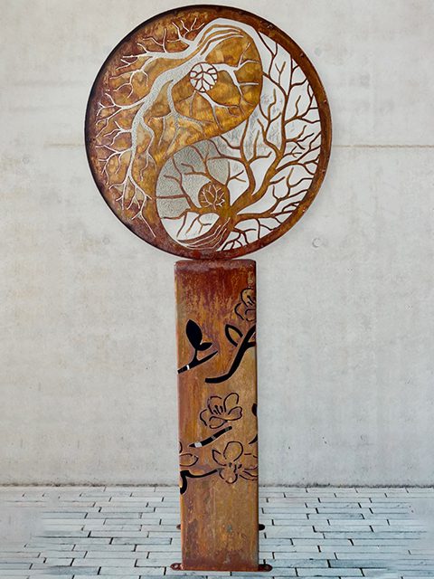 A large, intricate yin yang forest metal sculpture  stands prominently, showcasing its artistic design