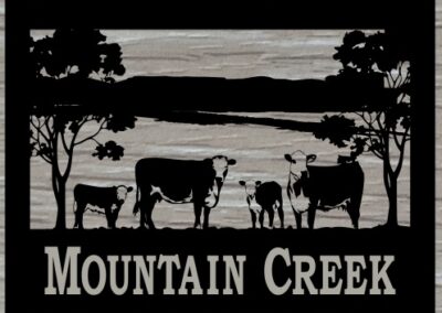 A sign indicating a mountain creek, surrounded by grazing cows and lush trees in a serene natural setting.