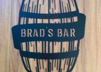 A rustic wooden sign displaying the name "Brad's Bar" in bold lettering, set against a natural background.