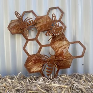 Rusted metal artwork of bees on hexagonal honeycombs against a corrugated background, placed on straw.