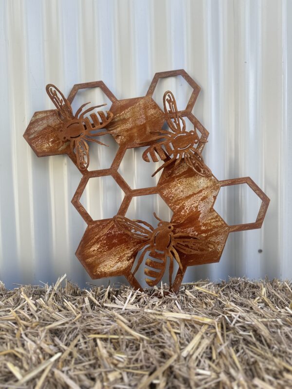 Rusted metal artwork of bees on hexagonal honeycombs against a corrugated background, placed on straw.