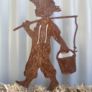 Rusty metal silhouette of a child carrying a lantern on a hay surface, with a corrugated backdrop.