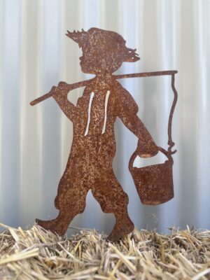 Rusty metal silhouette of a child carrying a lantern on a hay surface, with a corrugated backdrop.