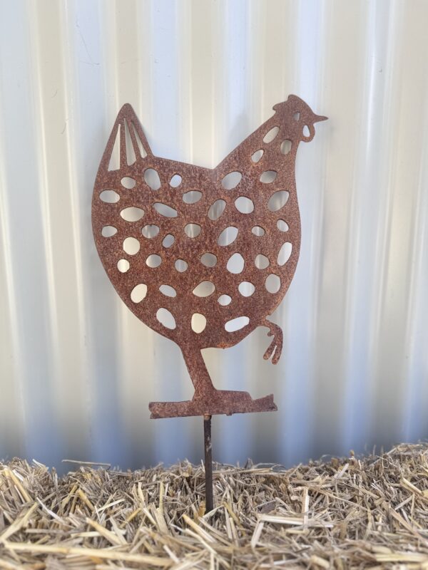 Rustic metal chicken silhouette garden ornament on a straw surface against a corrugated background.