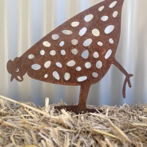 Rusty metal leaf-shaped cutout with bird design, standing on straw-covered ground.