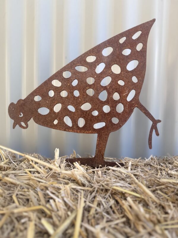 Rusty metal leaf-shaped cutout with bird design, standing on straw-covered ground.