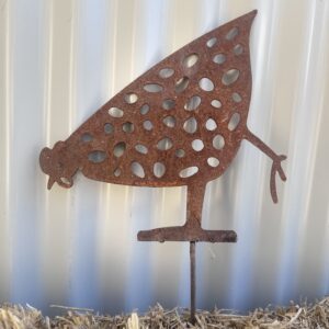 Rustic metal silhouette of a chicken with cut-out patterns, standing on straw against a corrugated background.