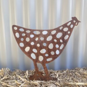 Rusted metal chicken silhouette with cut-out circles standing on straw against a corrugated wall.