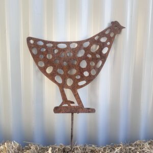 Rusted metal chicken silhouette with circular patterns on a straw bale against a corrugated wall.