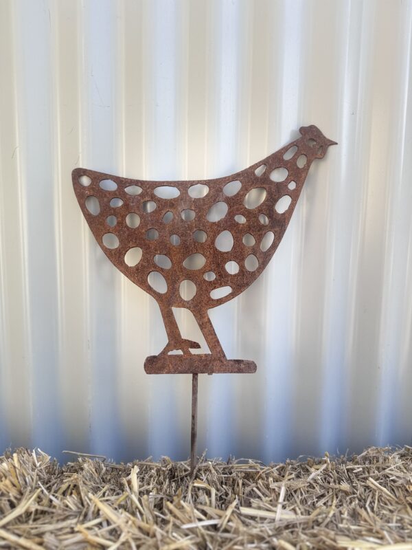 Rusted metal chicken silhouette with circular patterns on a straw bale against a corrugated wall.