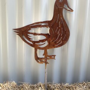 Rusty metal duck silhouette with artistic cut-outs, standing on straw against a corrugated wall.