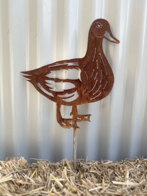 Rusty metal duck silhouette with artistic cut-outs, standing on straw against a corrugated wall.