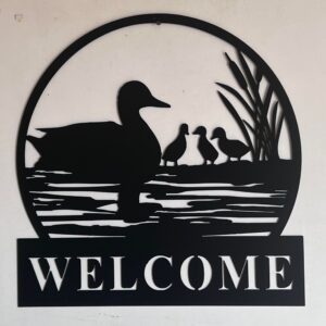 Black silhouette welcome sign featuring a duck in water with ducklings and reeds.