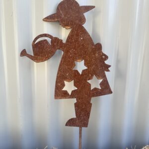 Rustic metal silhouette of a girl with a watering can, set against a ribbed wall, standing on straw.