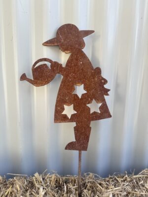 Rustic metal silhouette of a girl with a watering can, set against a ribbed wall, standing on straw.