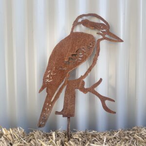 Rusty metal cutout of a bird perched, against a corrugated white background, standing on straw.