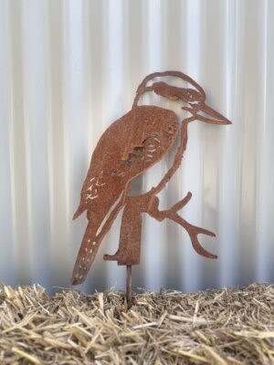 Rusty metal cutout of a bird perched, against a corrugated white background, standing on straw.