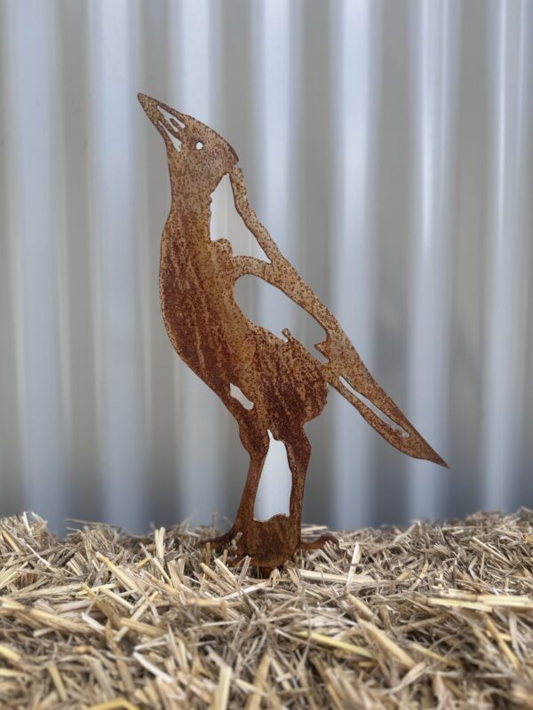 Rusty metal cutout of a penguin on straw, with a corrugated iron background.