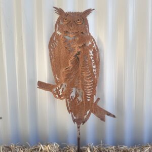 Rustic metal owl silhouette against a corrugated wall, mounted on straw-covered ground.