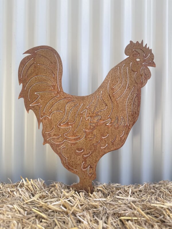 Rustic metal rooster silhouette on straw against a corrugated metal backdrop.