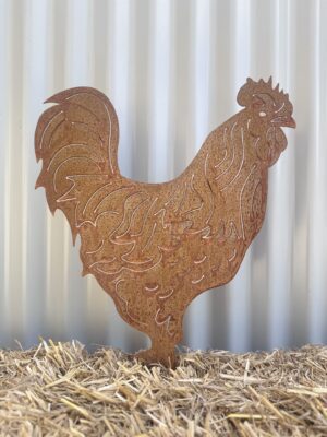 Rustic metal rooster silhouette on straw against a corrugated metal backdrop.