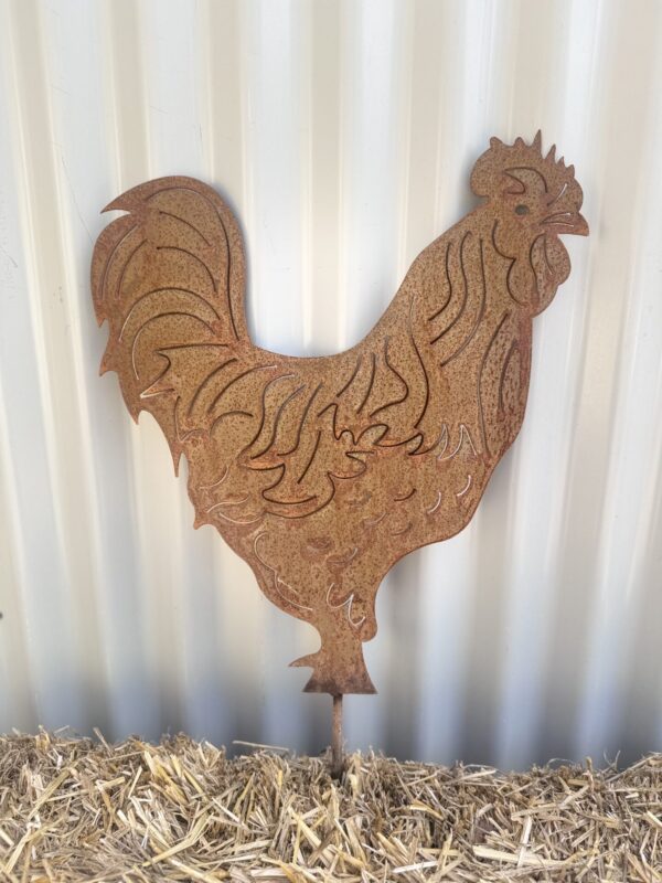 Rustic metal rooster silhouette against a corrugated wall, standing on straw.