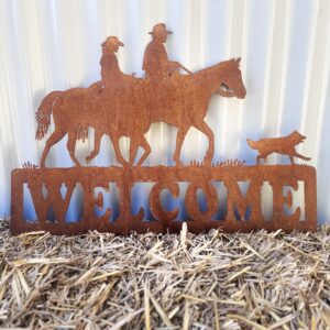 Rustic metal "WELCOME" sign with horse, rider, and dog silhouettes on straw, against a corrugated wall.