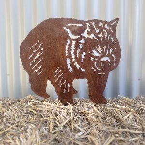 Rustic metal silhouette of a wombat with cut-out patterns on hay against a corrugated backdrop.