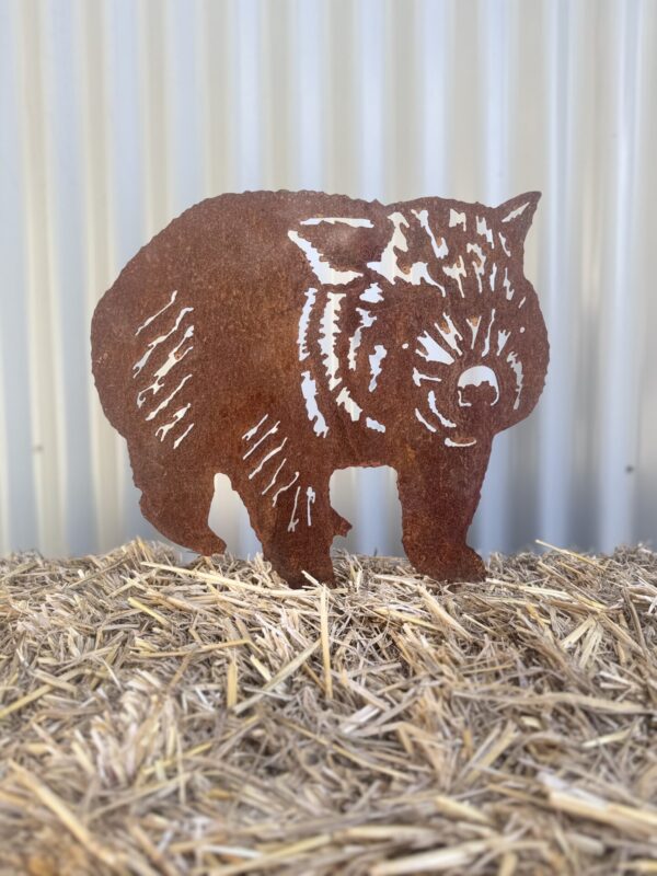 Rustic metal silhouette of a wombat with cut-out patterns on hay against a corrugated backdrop.