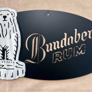 Metallic sign with a bear and "Bundaberg RUM" text on a black oval background.