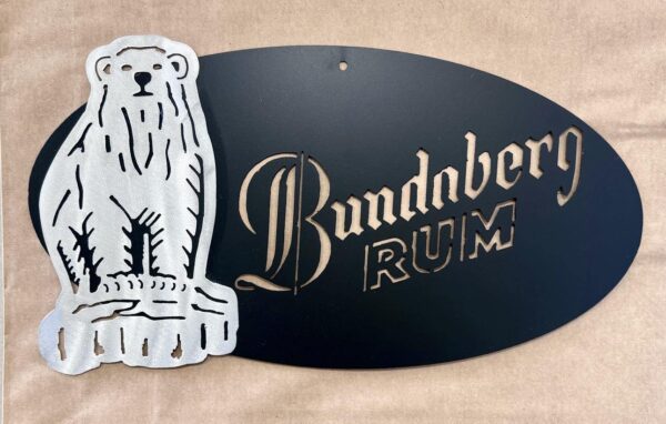 Metallic sign with a bear and "Bundaberg RUM" text on a black oval background.