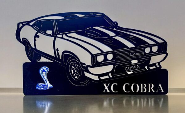 Black silhouette of a classic car with "XC COBRA" text and cobra graphic on reflective surface.