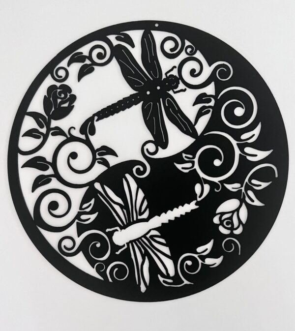 Black circular metal wall art with intricate floral and dragonfly design on a white background.